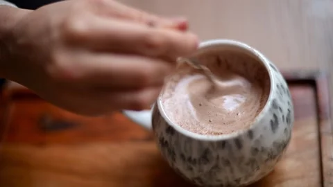Hand stirring hot chocolate inside a ceramic mug, creating creamy foam Stock Footage 325798383