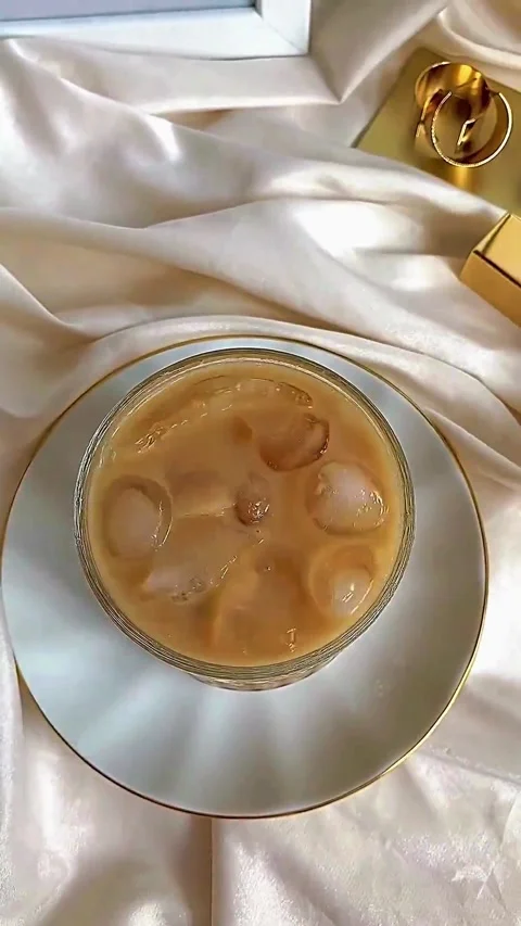 Hand stirring iced coffee in a glass cup on a white silk background Video stock 344615260
