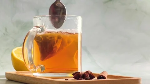 Hand stirring orange herbal tea with spoon in clear glass cup Stock Footage 336953595