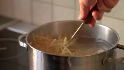 Hand stirring pasta in pan in which water stand on electric stove in kitchen Stock Footage 140338946