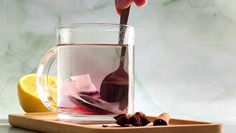 Hand stirring red herbal tea with spoon in clear glass cup, hot steam Video stock 336953728