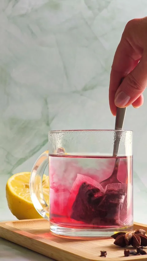 Hand stirring red herbal tea with spoon in clear glass cup, hot steam Video stock 336953804