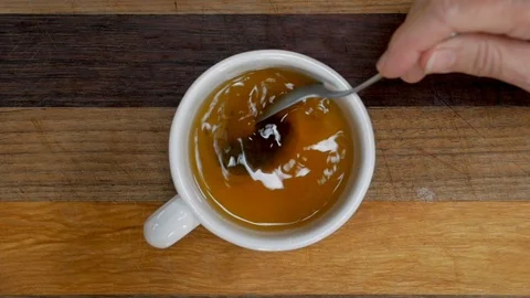 Hand stirring a tea bag in a tea cup with a spoon - slow motion overhead shot Video stock 93897041