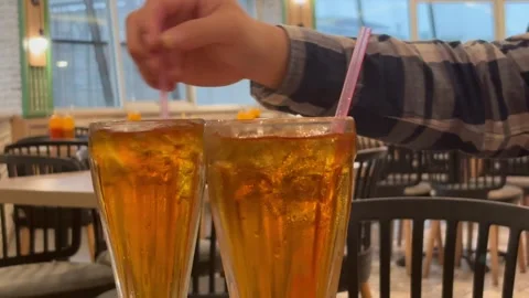 Hand Stirring Two Glasses of Fresh Iced Tea with Straws in a Restaurant Stock Footage 330145216