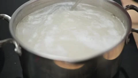 A hand stirs boiling rice in a pot using a fork. The pot sits on a stovetop as 库存影片 338298537