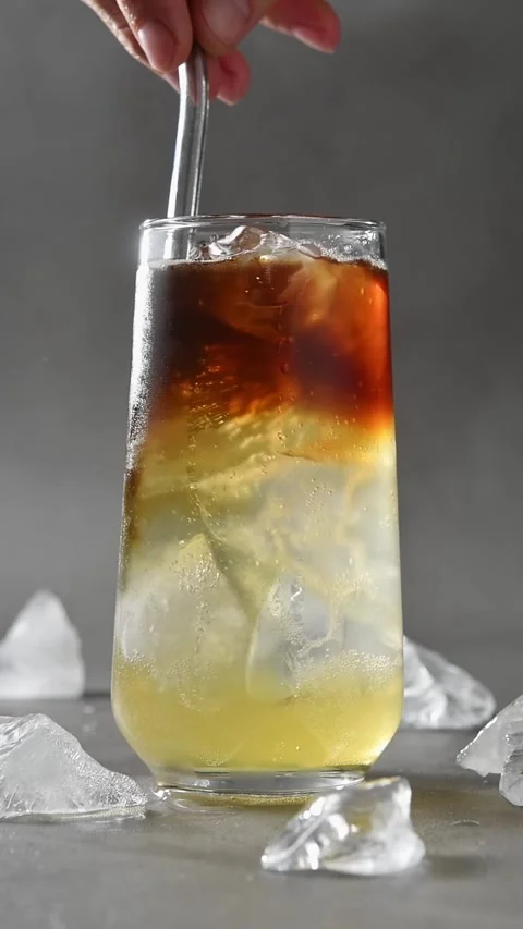 Hand stirs layered cold brew, apple cider and tonic with ice using metal straw Stock Footage 345487258