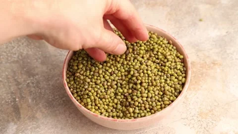 Hand stirs mung beans into a ceramic bowl on a brown concrete Video stock 221548576