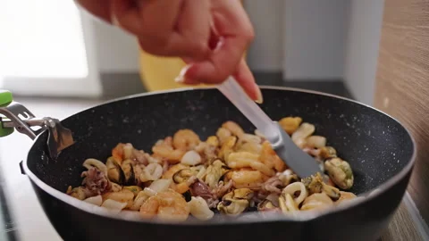A Hand Stirs Shrimp Squid and Mussels in a Black Wok, Preparing a Fresh Protein Stock Footage 341974889