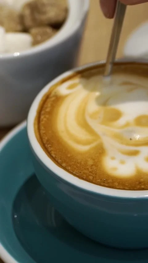 Hand stirs with spoon cooked coffee with latte art. Cup of cappuccino with foam Stock Footage 281164363