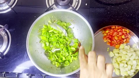 Hand stirs veggies in hot spiced oil over flame Stock Footage 305960639