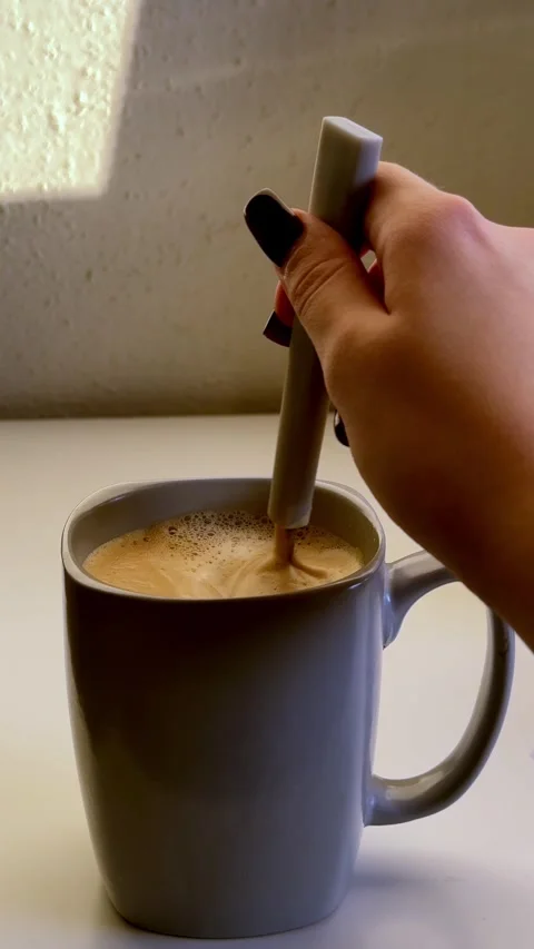 Hand stirs warm liquid within ceramic vessel, a morning ritual providing Stock Footage 334552058