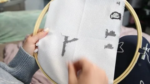 Hand stitching black cross stitch pattern on white fabric with wooden hoop .. Stock Footage 334955181