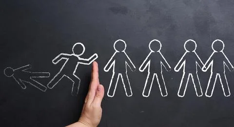 A hand stops a chain reaction of falling figures drawn in chalk on a blackb.. 库存照片