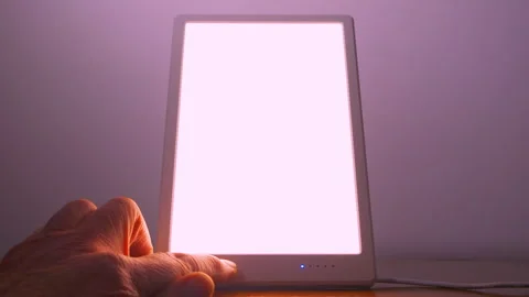 A hand switching on and adjusting a light therapy lamp. Video stock 260242429