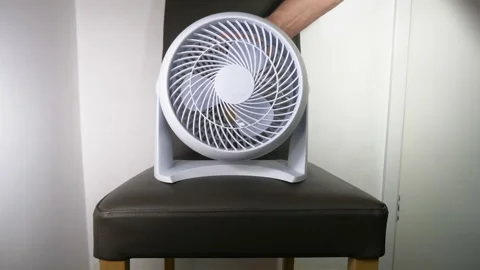 Hand switching on a small cooling fan, balanced on a chair. Video stock 200877388