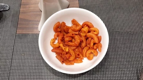 Hand Take Crispy Spicy Red Fried Macaroni Chips from White Bowl on Wooden Table Stock Footage 317944807