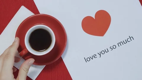 Hand take off put coffee in red mug on table with Valentine's postcard. Top view Vídeo Stock 121519024