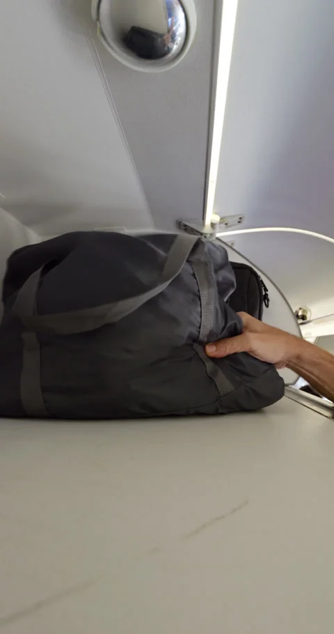 Hand take soft bag and laptop bag from overhead rack at economy class, then back Stock Footage 297053779