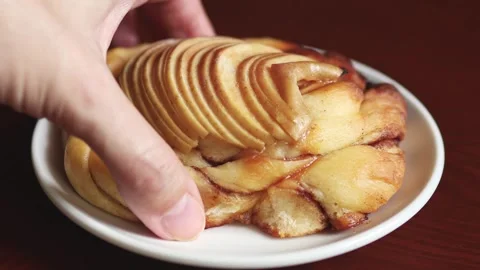 Hand takes apple cinnamon bun from white plate Video stock 346094339