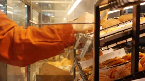 A hand takes baked goods through a glass bakery display window, reaching toward Stock Footage 330248570
