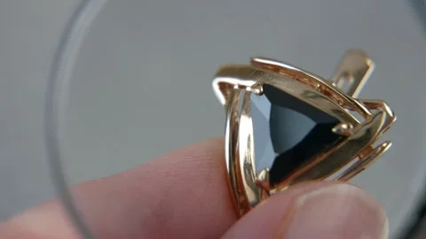 Hand takes earring with big black stone, jeweler looking at jewelry through.. Video stock 248304592
