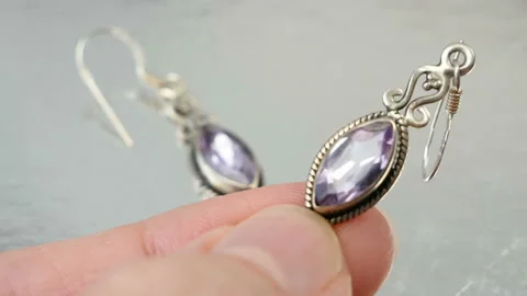 Hand takes earring with big violet amethyst, jeweler looking at jewelry throu Video stock 141798645