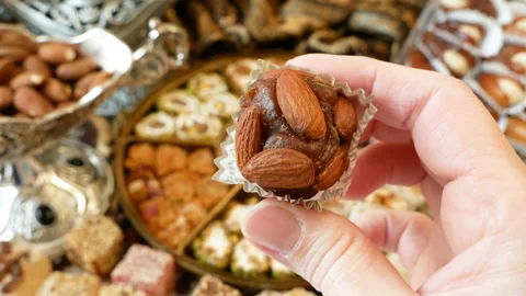 Hand takes eastern sweets with nuts,dates, candy in metal vase on wooden back Видео 142055400