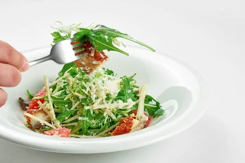 Hand takes an eel and grapefruit salad from a white plate on a white tableclo Stock Photos