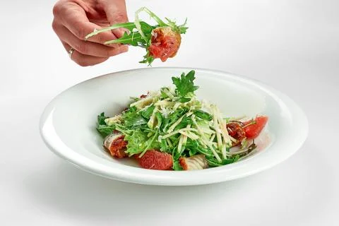 Hand takes an eel and grapefruit salad from a white plate on a white tableclo Stock Photos