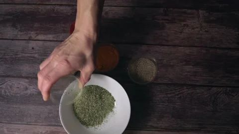 The hand takes jars of spices and pours them into one cup for stirring. Stock Footage 232137772
