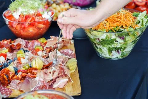 Hand takes meat snacks from meat platter on the buffet table during a festive Stock Photos