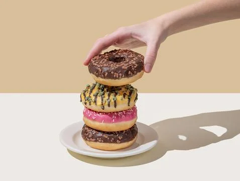 Hand takes one donut from stack of glazed donuts with different toppings on.. Foto stock