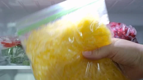 Hand takes a plastic bag of chopped yellow  carrots out of the freezer. 库存影片 341553865