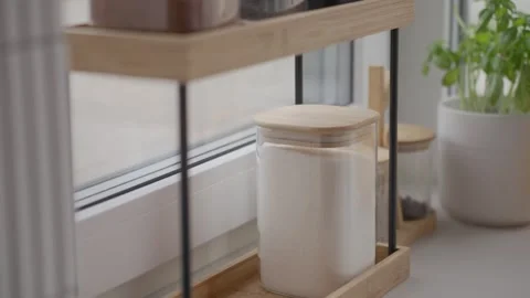 Hand takes salt and sugar jars from kitchen organizer near window Stock Footage 337737552