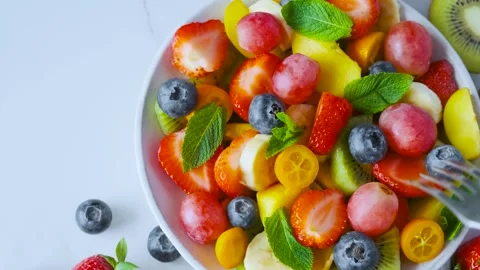 Hand takes strawberry with fork from bowl of summer colorful fruit salad. Top Stock Footage 315860239