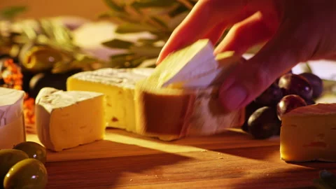 Hand Taking Bread Slice with Camembert Cheese from Rustic Board with Olives and Stock Footage 334269046