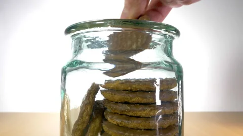 A hand taking a chocolate coated digestive biscuit from a storage jar. Video stock 271537268
