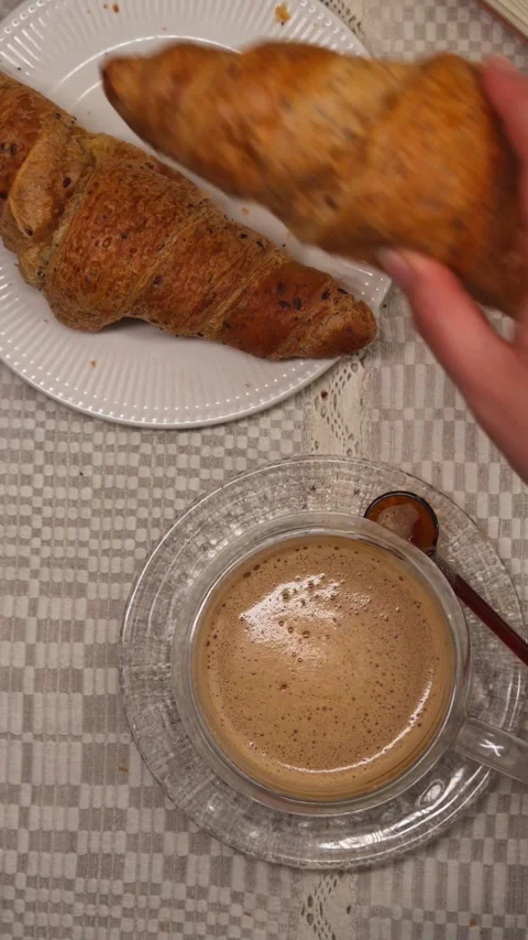 Hand taking croissant from plate beside cappuccino top view vertical video Stock Footage 335422467