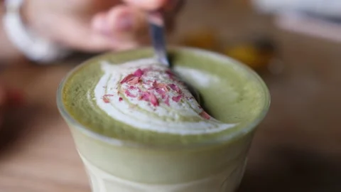 Hand taking foam off matcha tea latte decorated with the spoon and shows it to Stock Footage 150806991