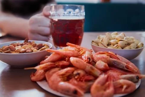 Hand taking a mug of beer on a table with nuts and shrimps, snacks in a beer  Stock Photos