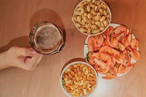 Hand taking a mug of beer on a table with nuts and shrimps, snacks in a beer  Stock Photos
