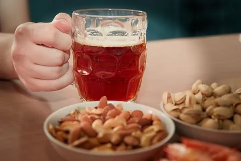 Hand taking a mug of beer on a table with nuts and shrimps, snacks for beer i Stock Photos