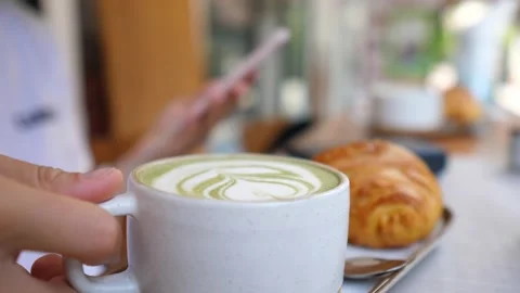 Hand taking mug with matcha green tea latte. Smartphone blurred in the Video stock 147859473