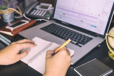 Hand taking note from Stock trading data on computer screen 库存照片
