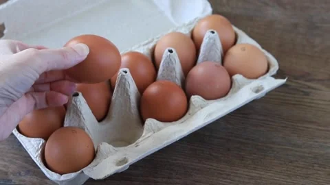Hand Taking Out Fresh Brown Chicken Egg from Cardboard Box on Wooden Table .. Stock Footage 346784739