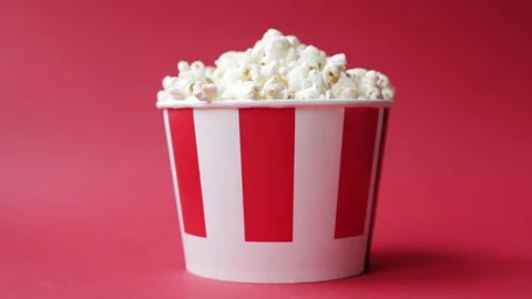  hand taking popcorn from striped red and white paper box on red background Stock Footage 126570422