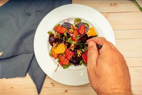 Hand taking a portion of the delicious beetroot, orange, walnut and arugula s Stock Photos
