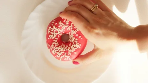 Hand taking red, pink donut from white plate, view from above Stock-Footage 124839996