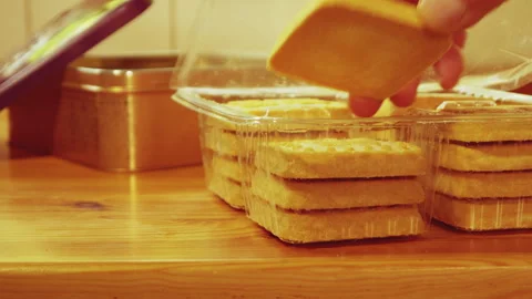 Hand taking shortbread biscuit from pack, next to tin container box and lid. Video stock 240211556