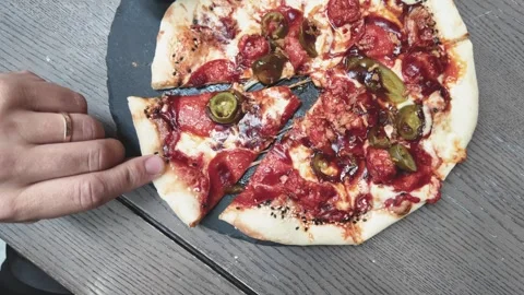 Hand Taking Slice of Fresh Pepperoni Jalapeño Pizza on Rustic Wooden Table Stock Footage 340536211